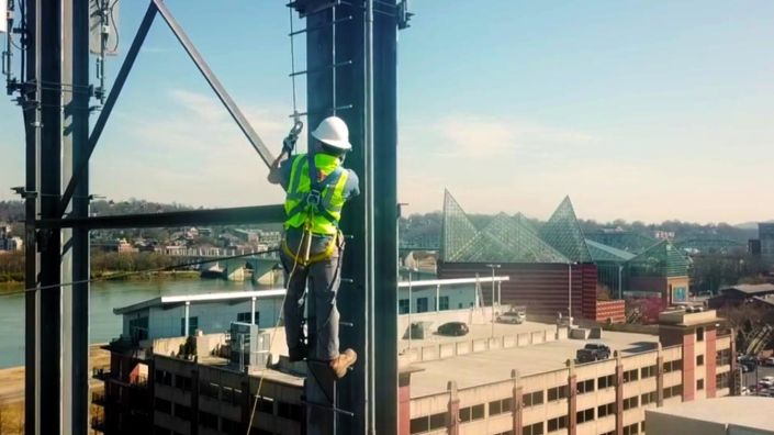 A Tri-State Electrical lineman in a safety harness working on a steel tower high above downtown Chattanooga